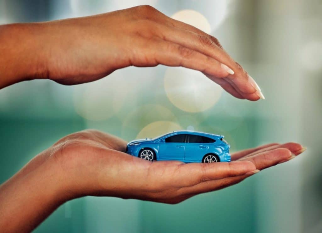 mains protégeant une miniature de voiture bleue – assurance et protection automobile