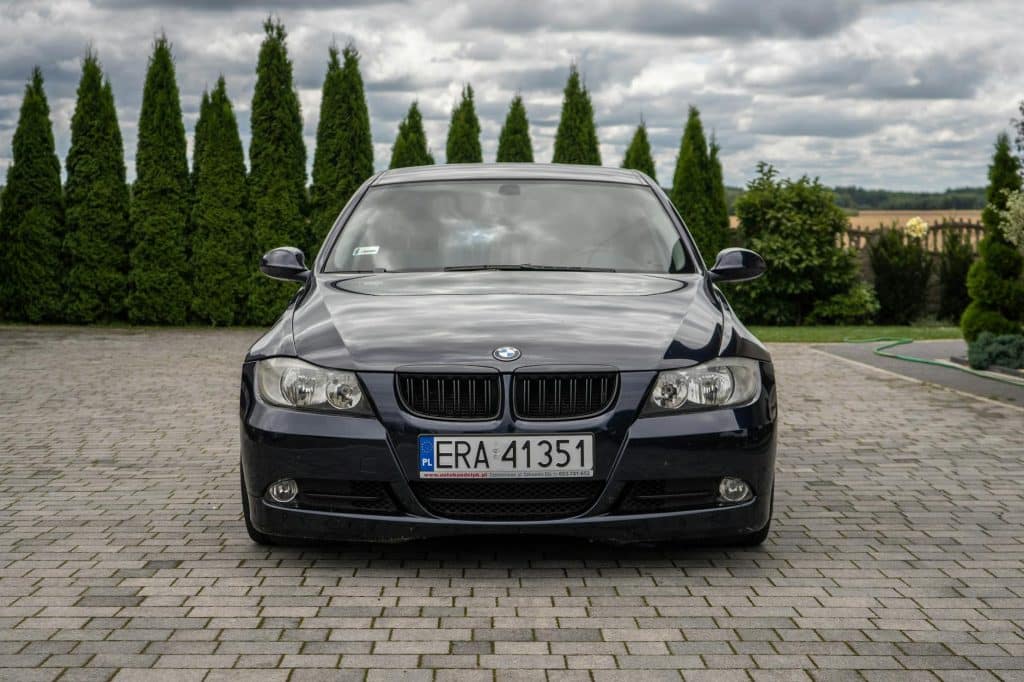 BMW Série 3 noire devant concessionnaire allemand avec drapeau